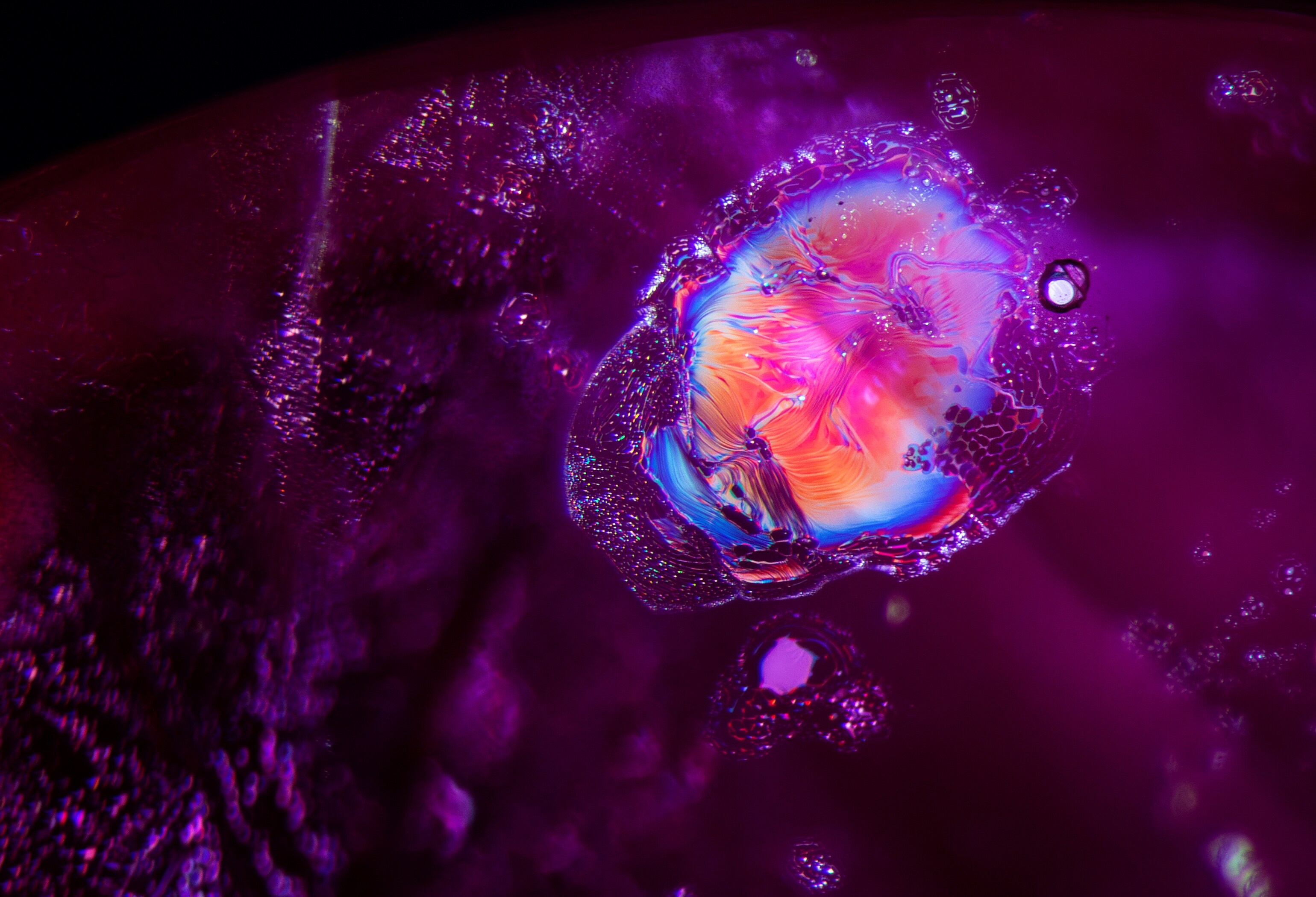 一块小型融化晶体与其薄膜内含物，在光纤照明下展现出耀眼色彩。©E. Billie Hughes, Lotus Gemology。